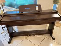 Front view of Technics digital piano showing cabinet, pedals, bench partially visible