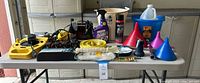 Overall view of table with battery charger, cord reel, ropes, buckets, funnels, cleaners, hardware