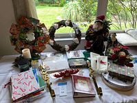 Overall lot on table displaying wreaths, figurines, towels, candles, hangers, tin, ornament box
