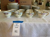 Front view of 12 teacups with floral pattern and gold handles