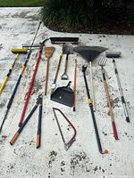 Full layout of all long-handled yard tools on driveway