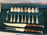 Ten large spoons, one small spoon, carving knife and fork laid on velvet tray