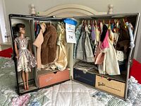 Open Barbie case displaying doll, clothing on hangers, drawers