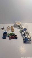 Group shot showing toy cars, gold lighter, car emblem, jewelry supplies bag and green plastic pieces