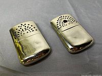 Two chrome metal pocket hand warmers, top view showing vent holes