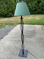 Full view of black metal floor lamp with green shade standing on driveway