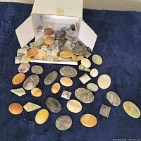 Open box displaying numerous polished flat-back stones spilling onto fabric