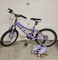 Full view of purple children’s bike and pair of quad skates