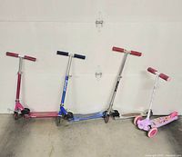 Four scooters lined up: three Razor folding kick scooters (pink, blue, red) and one Disney Princess tri-scooter