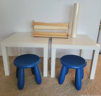 Two white tables, two blue stools, wooden paper roll holder, sealed roll