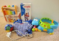 All items together showing xylophone bench on box, Evenflo jumper with harness and box, blue dinosaur ball popper with balls, segmented soft ball