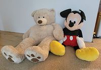 Teddy bear and Mickey Mouse plush side by side showing scale and condition