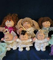 Group shot of three full-size Cabbage Patch dolls and three Snugglies angel dolls