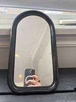 Front view of small arched mirror showing black frame and mirror surface