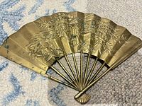 Front view of brass wall fan displaying phoenix and floral relief design and patina
