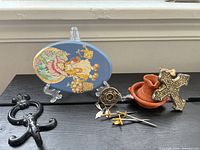 All items grouped: plaque, cross ornament, terracotta candle holder, cast-iron hook, sword pins