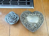 Rose-shaped metal trinket box beside heart-shaped ornate pewter lid
