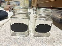 Front view of both square glass jars showing chalkboard labels and bail closures