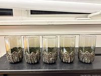 Five smoky glass tumblers with ornate silver-tone metal bases lined up