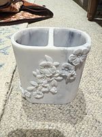 Front view of marbled resin toothbrush holder showing floral relief and overall shape