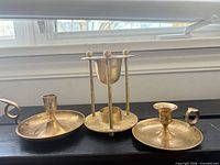 Front view of three brass candle holders showing two chambersticks and one candle warming stand