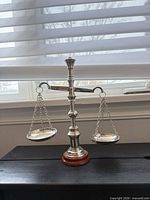 Front view of silver-tone decorative balance scale on wooden base showing both hanging pans and column