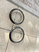 Two round clear glass coasters with starburst design and tarnished metal rims on tile floor