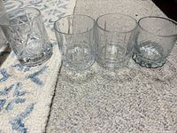 All four assorted clear whiskey tumblers shown upright on carpet