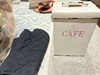 Canister with lid on, red 'CAFÉ' text, black trim, oven mitt beside