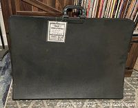 Front view of black vinyl portfolio with carry handle and attached product tag