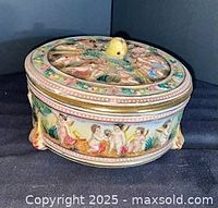 Side view showing round box, cherub relief, feet, gilt band