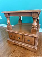 Full view of solid wood end table showing top, lower shelf, turned posts, drawer front