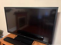 Front view of Sharp Aquos television on wooden stand with soundbar beneath screen