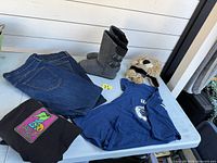 All items laid out: jeans, boots, black tee, blue tee, lion hat
