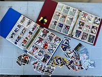 Two binders open showing pages of hockey cards with loose cards spread on table