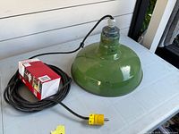 Full view of green porcelain pendant light, coiled cord, yellow plug and red box