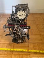 Front view of exposed punch clock mechanism with day dial and ribbon