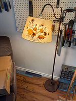 Full view of floor lamp beside sofa showing cast base, column, bridge arm and botanical shade