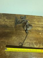 Overall view of cast iron dinner bell with bracket and ruler for scale