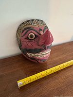 Front angled view of carved wooden mask with measuring tape for scale