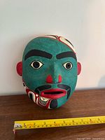 Front view of carved portrait mask with tape measure for scale