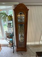 Full frontal view of grandfather clock showing entire wooden case, glass door, weights and pendulum