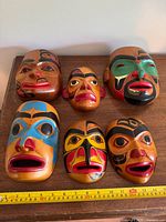 Six wooden masks laid out with measuring tape for scale