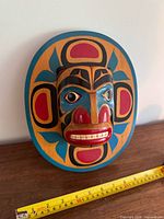 Front view of painted wooden mask with measuring tape for scale