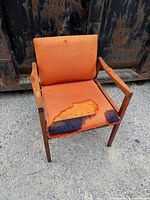 Front view of teak armchair showing torn orange upholstery