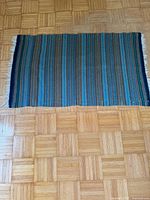 Full view of woven blanket on floor showing size, stripe pattern, fringe