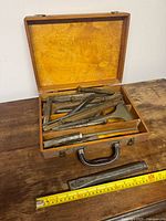 Closed wooden case with tools displayed and measuring tape for scale