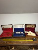Three open wooden cases displaying carving tools and coping saw