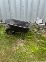 Full side view of black wheelbarrow, plastic tray, front tire, steel frame