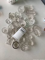 Group shot of assorted clear glass salt cellars with label slip and sterling-rimmed piece visible